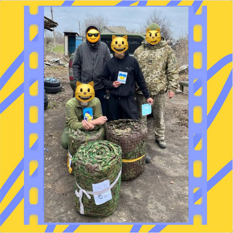 Four Defenders with emoji-covered faces hold postcards beside rolls of camouflage netting, in a blue and yellow frame